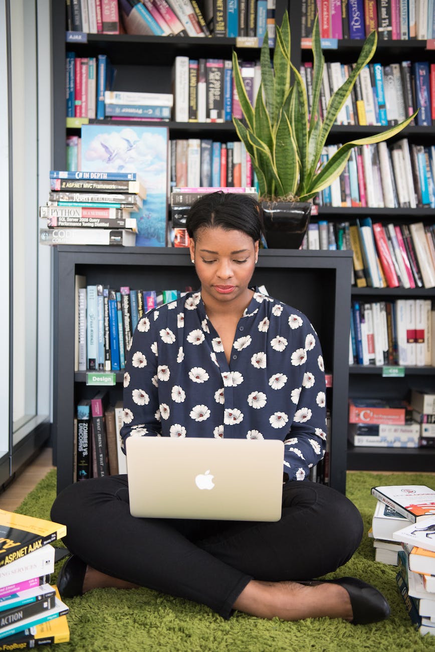 woman sits on floor facing gold macbook